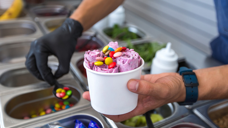 A street vendor adding candy toppings to a tub of rolled ice cream