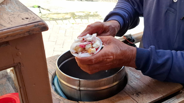 A vendor holding a tub of es puter ice cream over a metal bucket