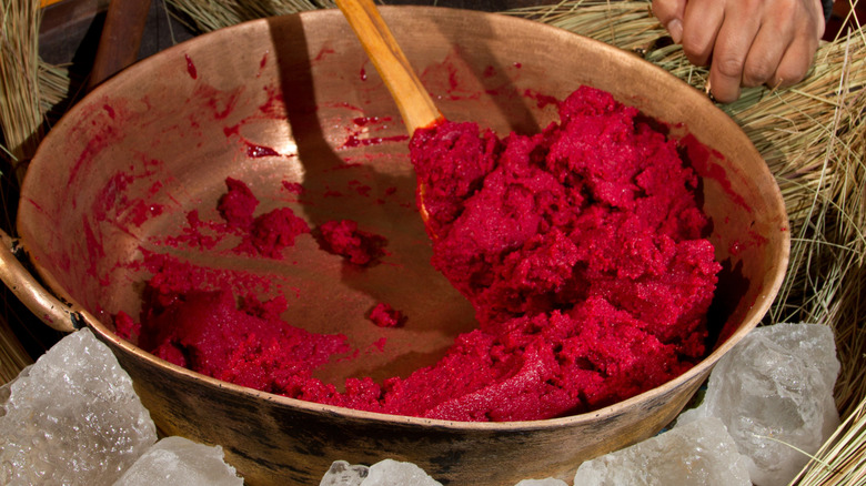 A person stirring bright red helado de paila ice cream in a copper wok
