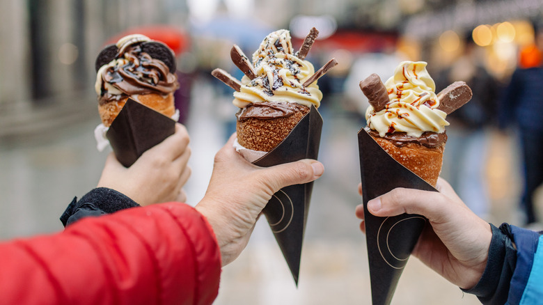 Three hands holding up ice creams in chimney cakes