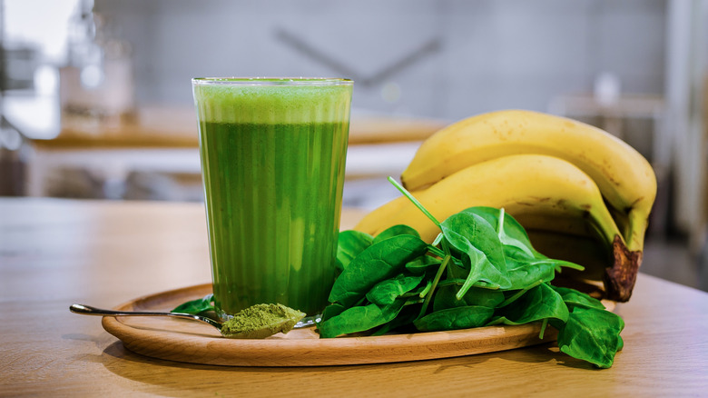 Green smoothie on platter with spinach, bananas, and spoonful of matcha powder