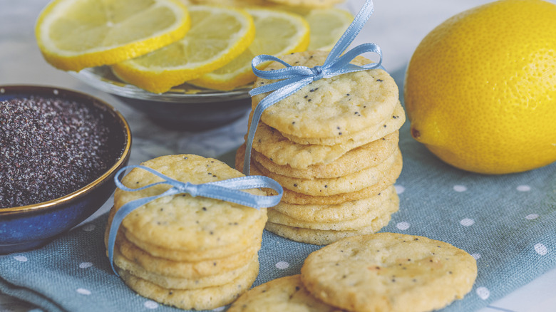 Lemon poppy seed cookies topped with ribbons next to lemon and bowl of poppy seeds