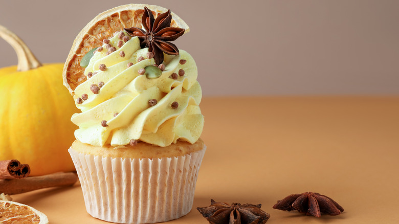 Cupcake topped with frosting, star anise, pumpkin seeds, and a dried orange slice