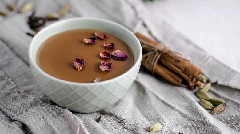 Masala chia pudding in bowl topped with rose petals and surrounded by cinnamon, cardamom, and cloves