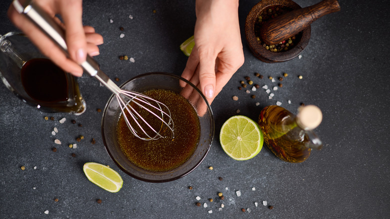 Hand whisking marinade in glass bowl next to sliced lime and soy sauce