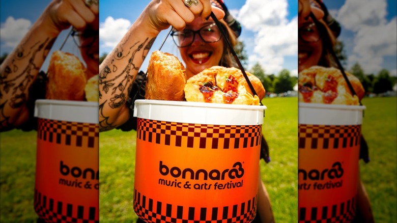 A person holding up food to the camera in a branded Bonnaroo bucket