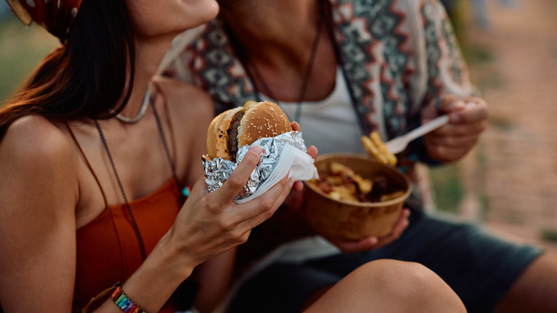 Two people sat next to each other outdoors in a festival-like setting enjoying food