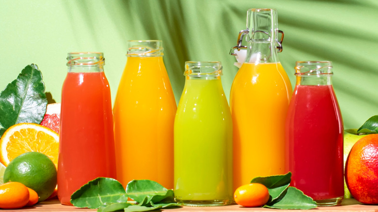 glass bottles filled with various flavors of juice, surrounded by citrus
