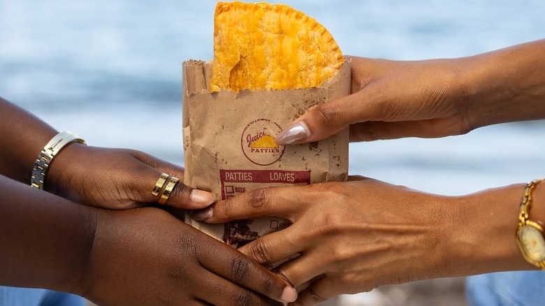 People handing each other Juici Patties on a beach