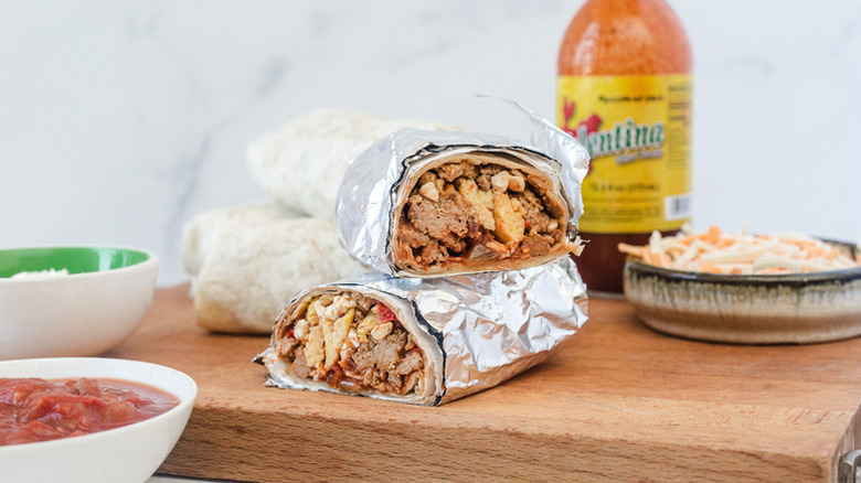 Halved, foil-wrapped breakfast burrito on wooden cutting board