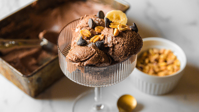 Scoops of chocolate peanut butter ice cream in glass, topped with peanuts and chocolate chips