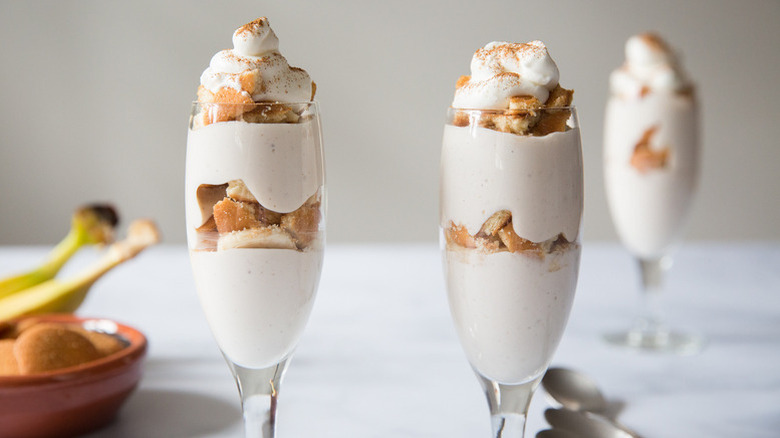 Two glasses of layered banana pudding dessert topped with whipped cream