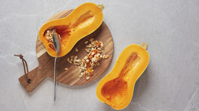 a halved butternut squash on a wooden tray with the seeds being scooped out