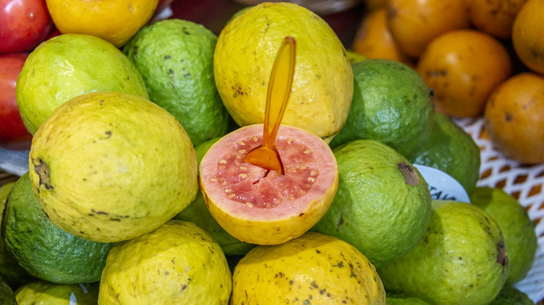 a pile of yellow and green guava fruits with one cut in half and a spoon sticking out