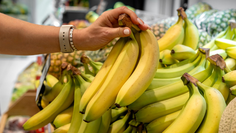 a hand picking up a bunch of bananas at the grocery store