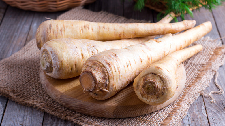 whole parsnips on a wooden round on top of a woven mat