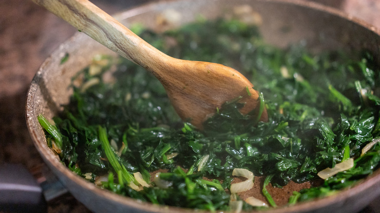 spinach cooking in a pan with wooden spoon