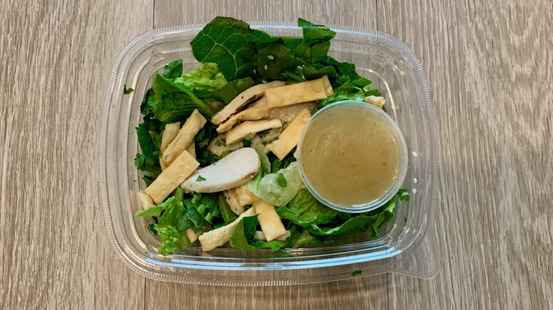 Top view of  Asian Sesame Chicken Salad in a plastic container with dressing