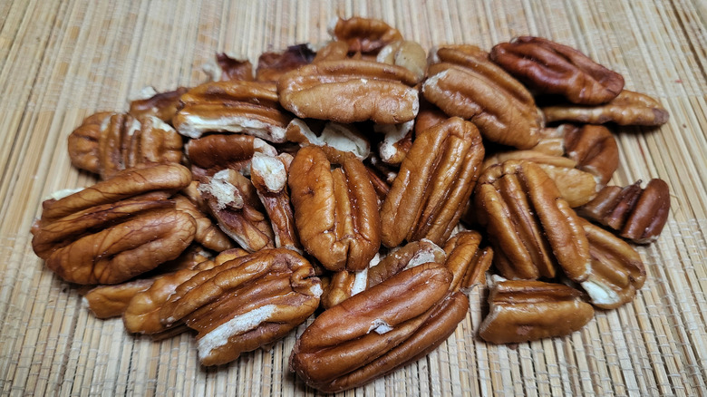 A pile of raw pecans on a natural, dried grass mat