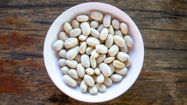 Small, white beans in a white bowl on a wood background