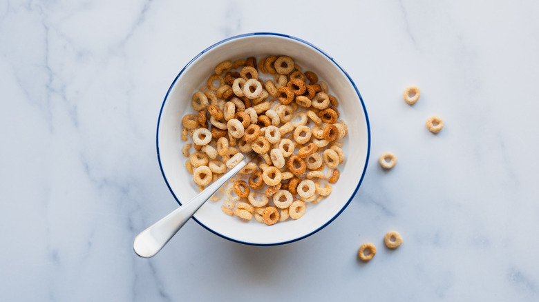 A bowl of cheerios with milk and a spoon.