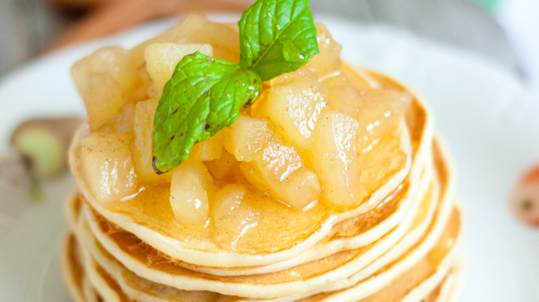 Close up of stack of pancakes topped with cooked apple chunks and mint sprig