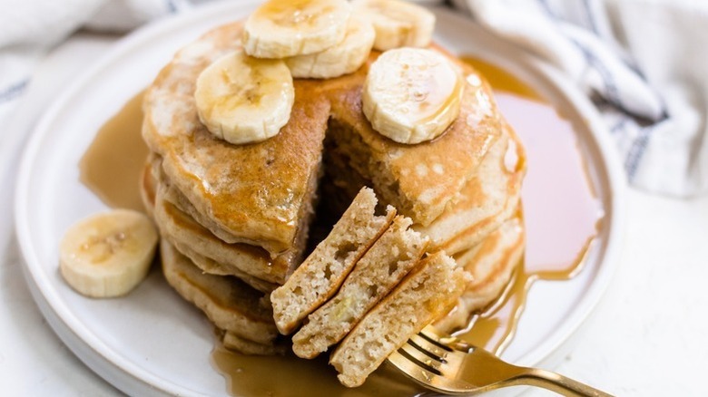 Stack of banana pancakes on plate with forkful taken out