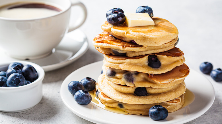 Stack of blueberry pancakes of plate with syrup and butter
