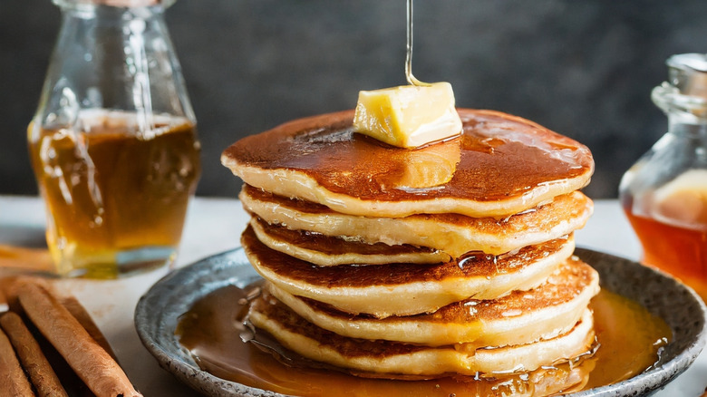 Stack of pancakes on plate next to cinnamon sticks
