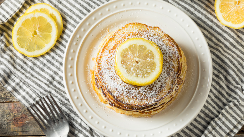 Stack of lemon ricotta pancakes on plate with fresh lemon rounds