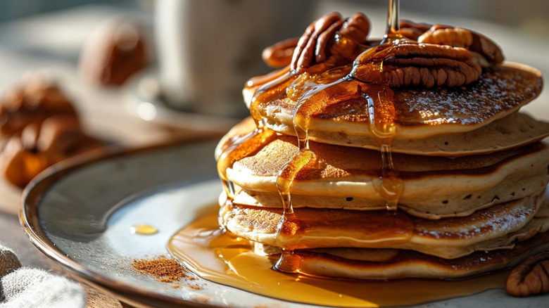 Stack of pecan pancakes being drizzled with maple syrup