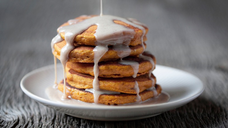 Pouring glaze over stack of pumpkin pancakes