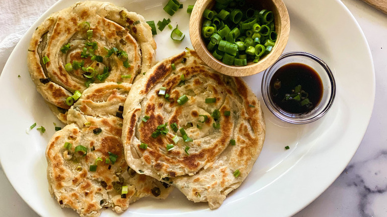 Plate of scallion pancakes served with extra scallions and soy sauce