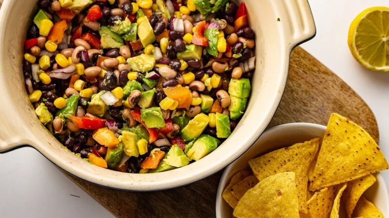 Bowl of cowboy caviar beside bowl of tortilla chips and a lemon half