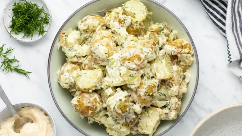 Creamy dill potato salad in bowl with extra dill and mayo on the side
