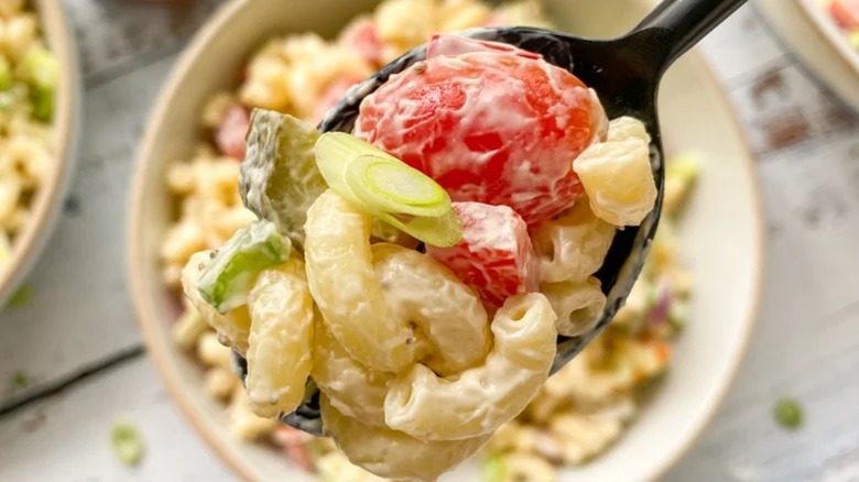 Spoonful of macaroni salad above bowl of macaroni salad
