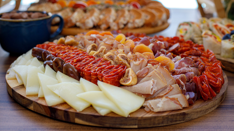 Multiple charcuterie boards with meats, cheeses, wraps, fruit, and chocolate pretzels