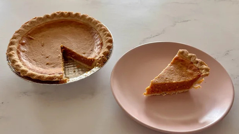 Bakery pumpkin pie slice on a plate next to a whole pie