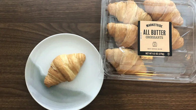 All butter croissants in packaging with one croissant on a plate next to it