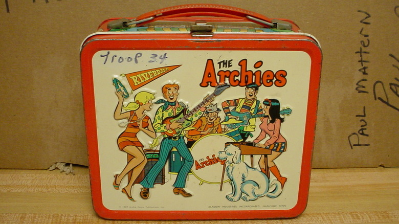 A used "The Archies" lunchbox from 1969 on a wooden table