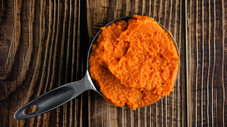 A metal measuring cup full of canned pumpkin puree on a brown natural background