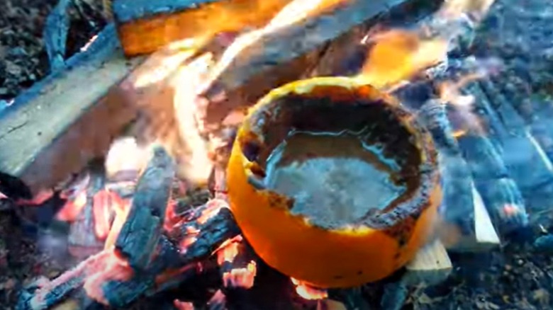 Coffee brewing inside an orange shell on a campfire