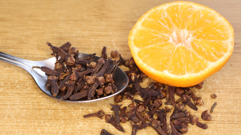 Whole cloves in a spoon and half an orange on a light-colored wood table