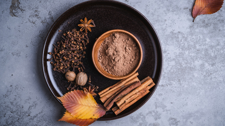 A black plate with whole and ground spices and autumn leaves on a slate table