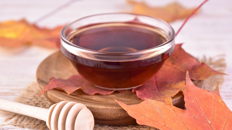 Maple syrup in a glass bowl on a wood platform surrounded by leaves