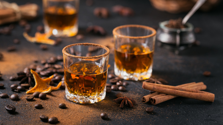 Two shot glasses of whiskey with coffee beans and spices on a dark backdrop