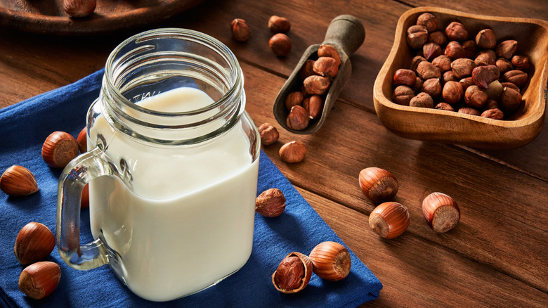 A glass of hazelnut milk on a wooden table surrounded by hazelnuts