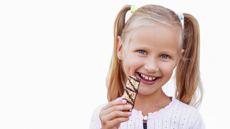 Young girl with pigtails eating granola bar drizzled in chocolate