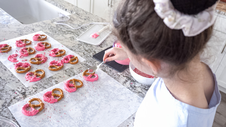 Young girl decorating pretzels with chocolate and sprinkles