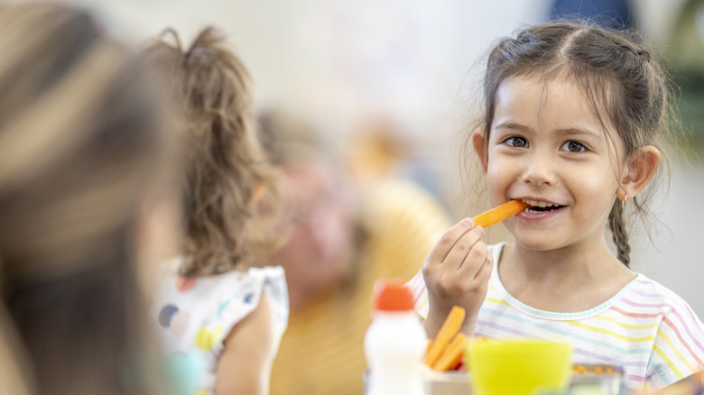 Young girl eating vegetables and looking into camera